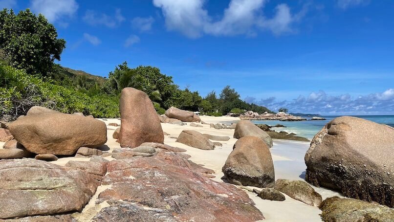 Rounded Seychelles rocks on white sandy beach, blue sky and sea in background